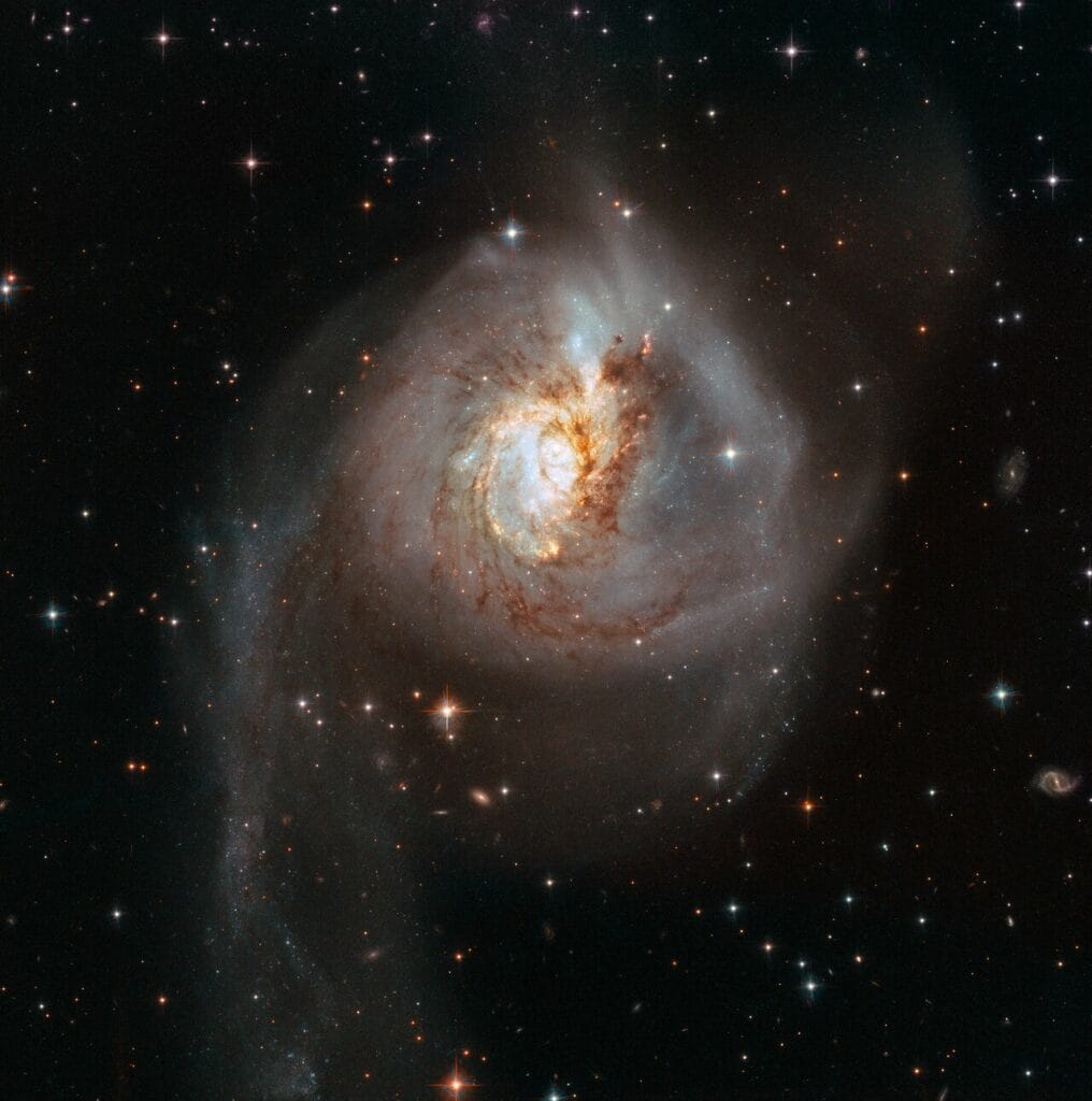Kolorowe, wysokorozdzielcze zdjęcie galaktyki NGC 3256 pokazujące jej zniekształconą strukturę po zderzeniu, z licznymi obszarami gwiazdotwórczymi świecącymi na czerwono i pomarańczowo (pył i gaz podgrzany przez młode gwiazdy).
