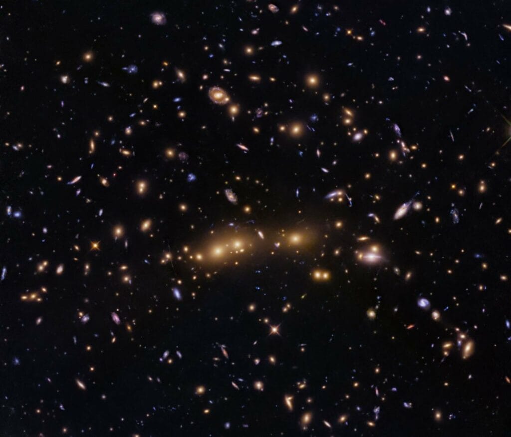 Kolorowa mozaika Hubble’a przedstawiająca gromadę CL0016+1609/MACS J0018.5+1626, z widocznymi jasnymi galaktykami eliptycznymi w centrum oraz słabymi, wyciągniętymi łukami soczewkowanych galaktyk tła