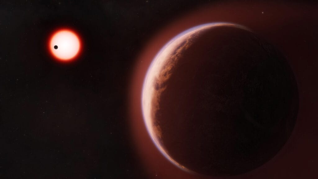Skalista egzoplaneta spowita mgławicową, niebieskawą poświatą atmosfery na tle ciemnego kosmosu, w oddali czerwony karzeł