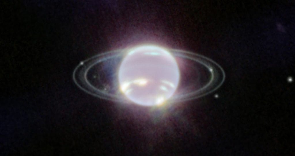 Ciemnoniebieska planeta Neptun otoczona delikatnymi, jasnymi pierścieniami na tle czarnego kosmosu usianego gwiazdami.
