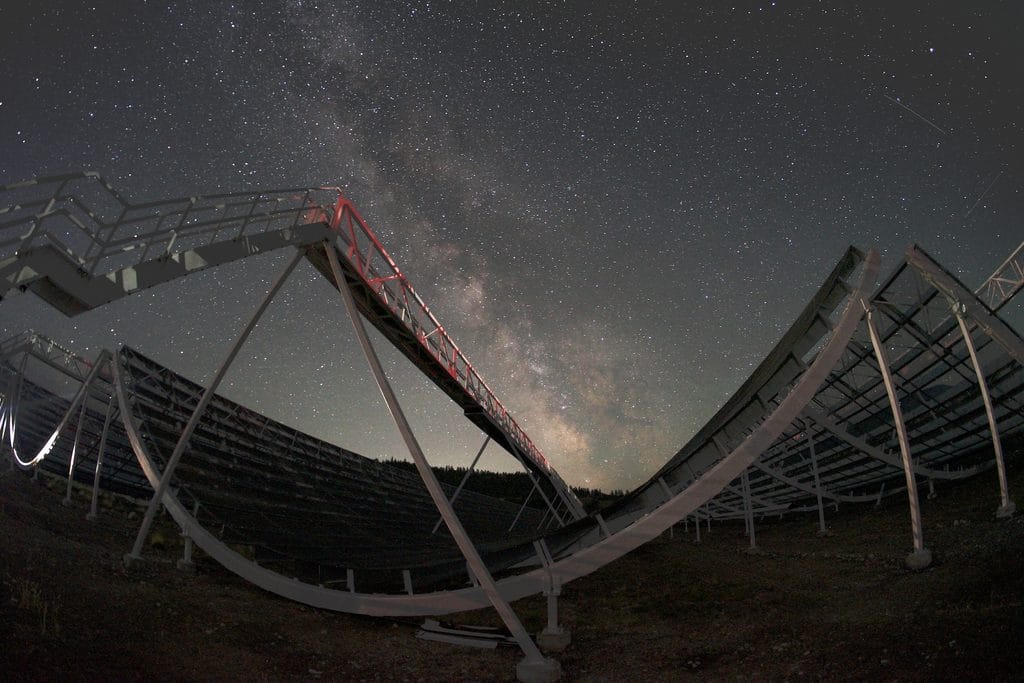 Nocne ujęcie radioteleskopu CHIME w pobliżu Penticton w Kolumbii Brytyjskiej. Na pierwszym planie widoczne są cztery charakterystyczne, nieruchome cylindryczne reflektory instrumentu, a nad nimi rozciąga się gwiaździste niebo z wyraźnym pasmem Drogi Mlecznej.