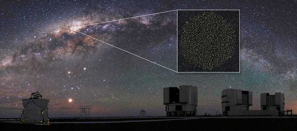 Panoramiczne zdjęcie nocnego nieba nad obserwatorium astronomicznym. W tle widoczna jest jasna wstęga Drogi Mlecznej, usiana gwiazdami. Na pierwszym planie znajdują się białe kopuły i budynki teleskopów na pustynnym płaskowyżu. Białe linie wskazują fragment Drogi Mlecznej, który powiększono w prostokątnym okienku w prawym górnym rogu. W powiększeniu widać rozkład około tysiąca punktów oznaczających cele obserwacyjne instrumentu MOONS